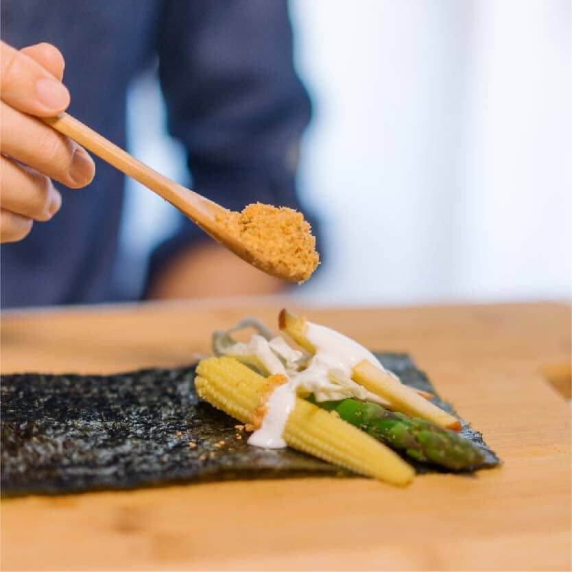 在壽司海苔上依序擺上⾼麗菜絲、苜蓿芽、蘆筍、玉米筍、蘋果絲和希臘優格，在最上⾯撒上素肉鬆。