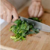 將芥蘭菜去掉表層纖維和花朵後，分別將莖部和葉切細，並先炒過芥蘭菜葉備用。