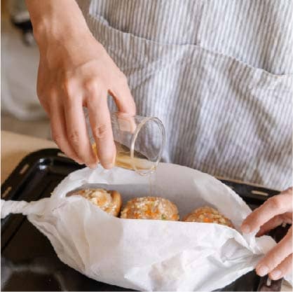 將香菇鑲肉置入烘焙紙中，抓起烘焙紙兩端旋轉塑形出筒狀；再將滴雞精倒入烘焙紙中並收口。送入已預熱至180度的烤箱烘烤20分鐘。