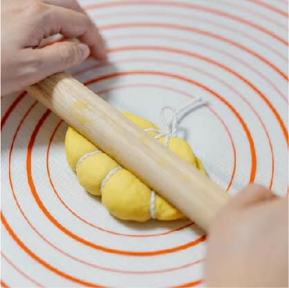 將大麵糰分成6等份擀成橢圓(1份約70-80g)，簡開兩端塑形繼續擀開；刷油對折再稍擀開一些，以棉繩塑形出南瓜線條用擀麵棍壓印。