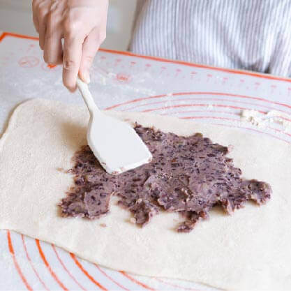 將堅果搗碎後與紅豆餡拌匀，平鋪在糯米麵糰上。
