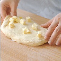 將麵團拍平展開，平均放上軟化的無鹽奶油丁包覆，分成兩份揉麵10分鐘後，合併麵團並封膜發酵1小時，中途翻面一次。