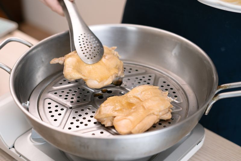 夾起鍋中的雞腿排，並裝入便當盒內。