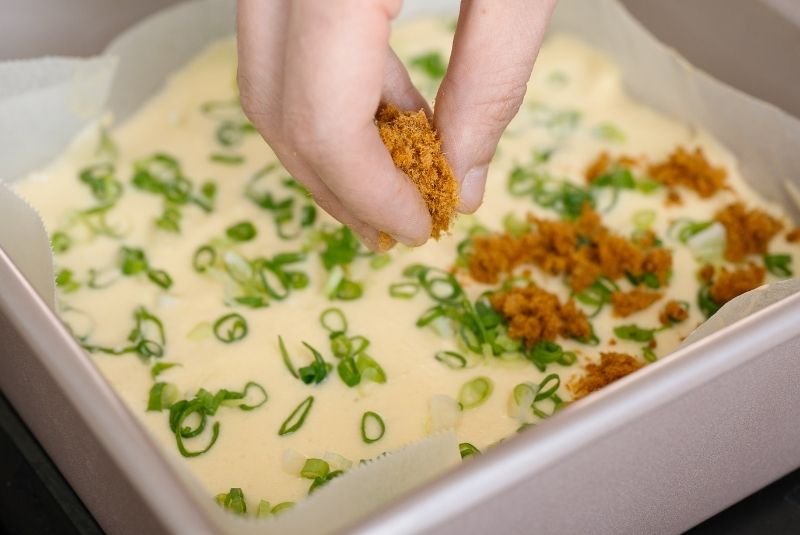 倒入放置烘焙紙的方形模具後，平均放上蔥花後，半邊撒上新東陽精緻豬肉鬆。