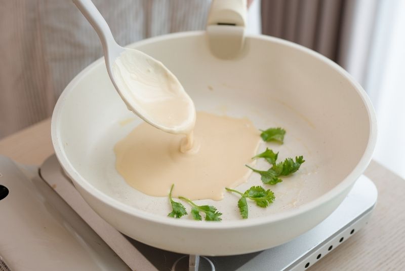 薄抹奶油至平底鍋後放上香菜，舀入麵糊，維持香菜在底部，接著開火以小火慢煎至底部上色。